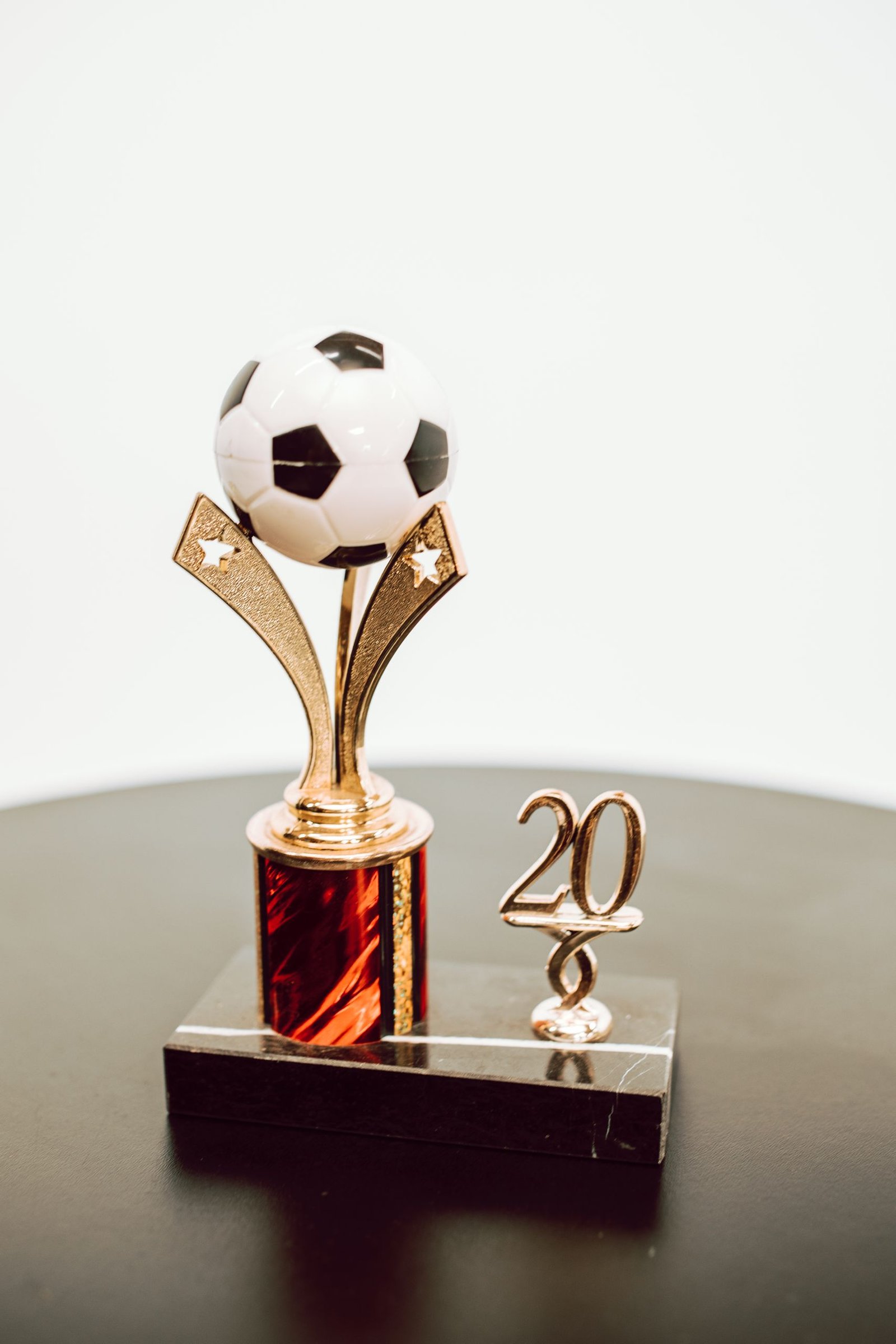 Shiny golden soccer trophy with ball and the year 20 on black surface.
